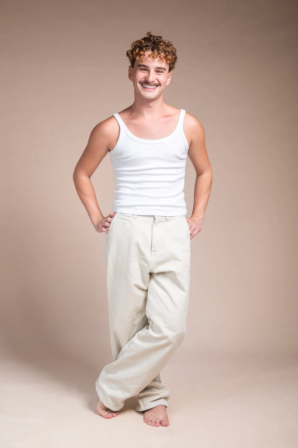 Homem de regata branca e calça clara, descalço, em pose de corpo inteiro